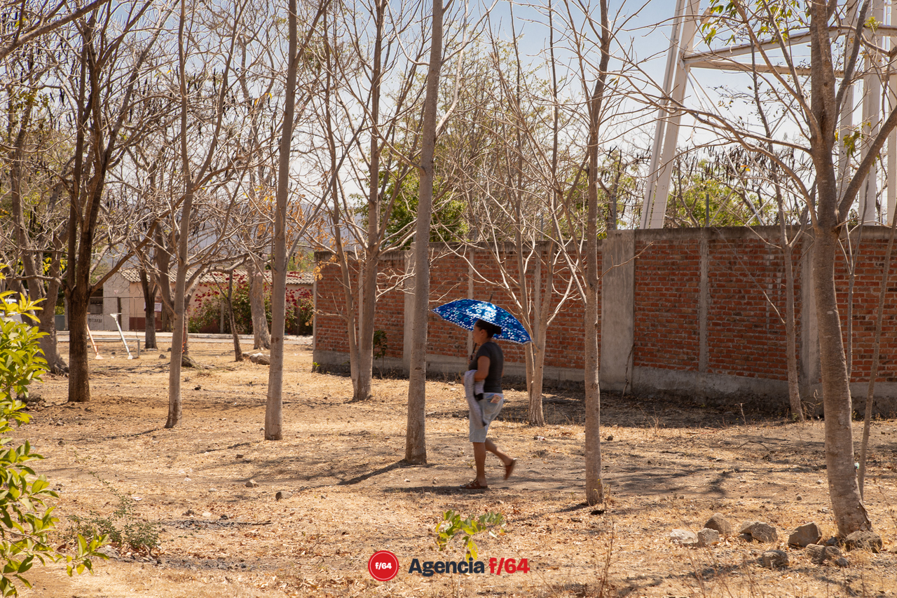 Habitante de la comunidad de El Amarradero, cruza por el Jardín de la comunidad bajo el intenso sol cubriéndose con un paraguas